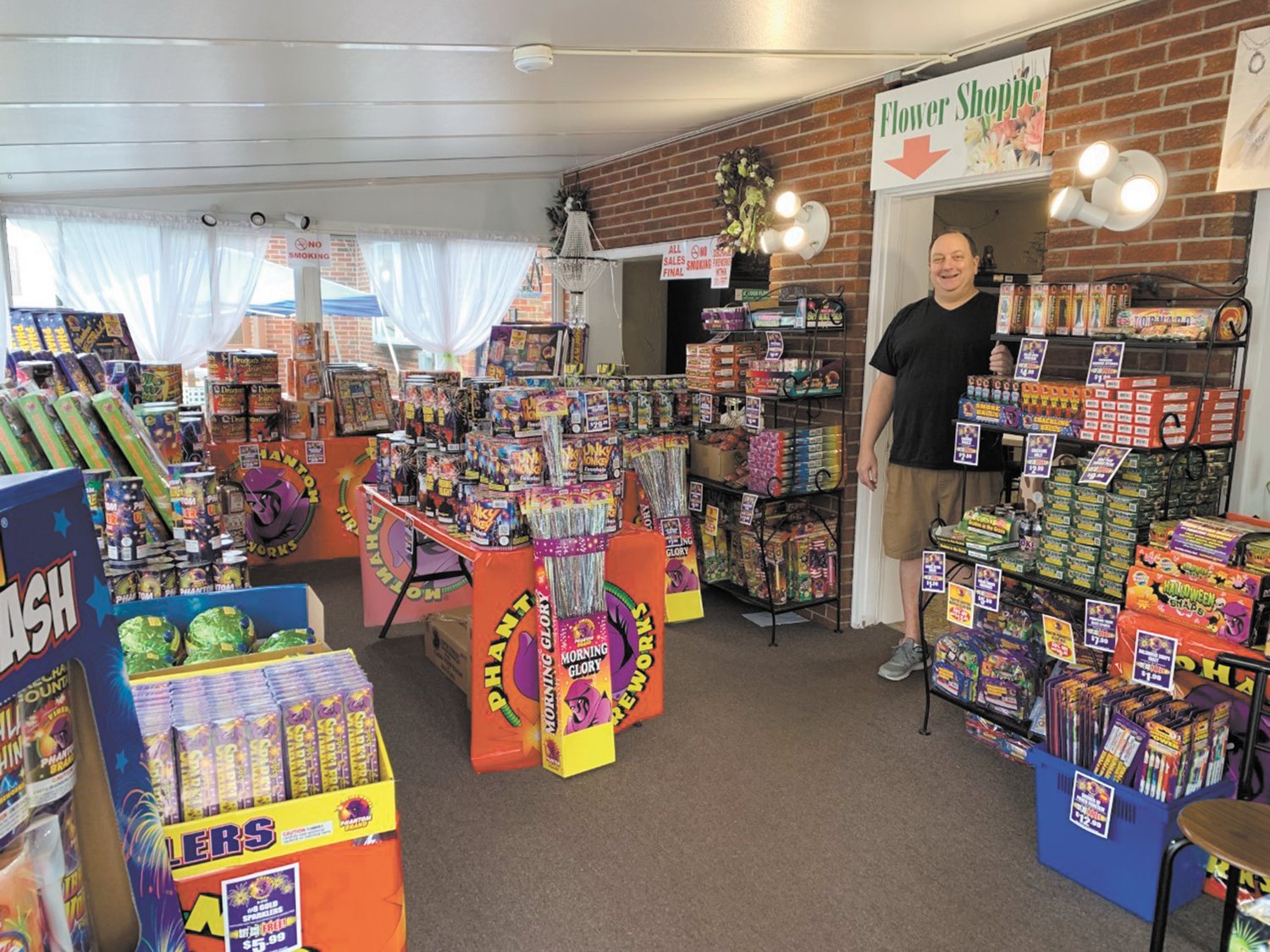 John Dick, the owner of Atwood Florist on Atwood Avenue, is seen here surrounded by some of this huge selection of fireworks ~ featuring fireworks by Phantom Fireworks. Be the best hostess this summer and kick-off the season with a visit to John!
